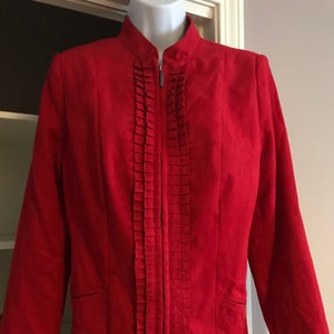 May include: A bright red jacket with a mandarin collar and a vertical pleated design down the front. The jacket has a zipper closure and two small pockets. The sleeves are long and the jacket is displayed on a white mannequin.