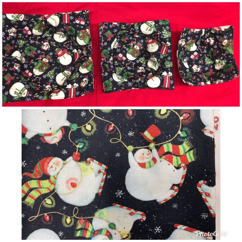 May include: Three black fabric cozies with a snowman pattern. The cozies mare different sizes and have a white background with red, green, and black accents. The fabric is quilted,has a soft texture. and is safe to use in the microwave