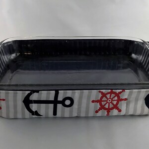 May include: A glass baking dish with a navy blue and white striped fabric cover. The fabric has a nautical theme with anchors and ship wheels.