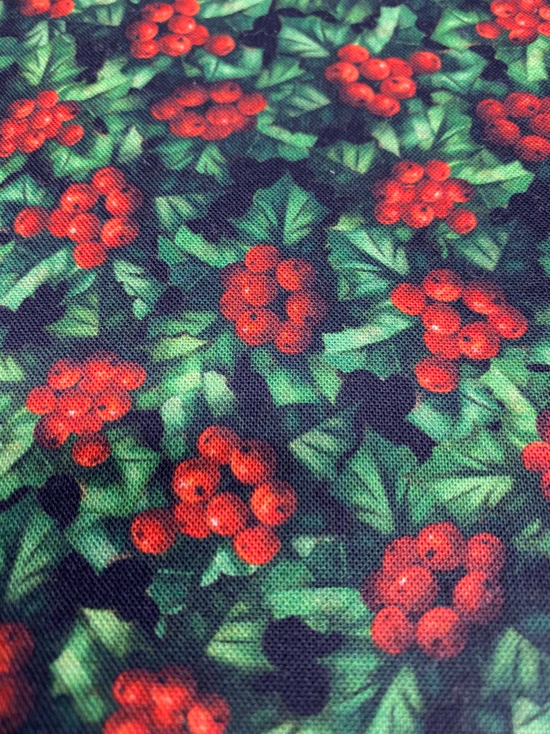 May include: A green fabric with a repeating pattern of red berries and green leaves. The fabric has a textured surface.