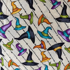 May include: A repeating pattern of colorful witch hats in various colors, including orange, green, purple, and blue, on a cream-colored background. The hats are outlined in black and arranged diagonally with black lines.