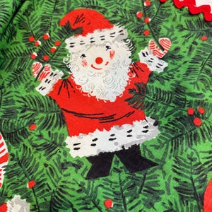 May include: A festive Christmas fabric featuring a cheerful Santa Claus illustration. Santa is dressed in a red suit with white trim, surrounded by green pine needles and red berries. A red, scalloped edge borders the fabric.