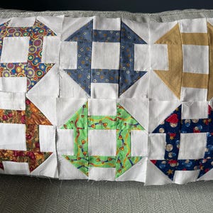 May include: A patchwork quilt top featuring six blocks with a repeating arrow and square design. The blocks showcase various patterned fabrics, including colorful circles, blue floral, and autumnal fruit designs, set against white squares.