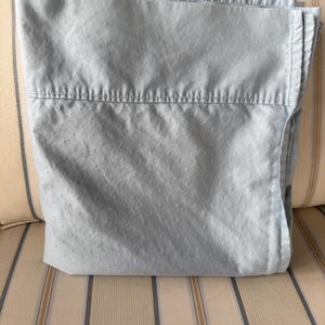 May include: A folded, light blue bed sheet with a subtle dotted pattern. The sheet is neatly folded, showcasing the top hem with visible stitching. The fabric appears soft and slightly textured, suggesting a comfortable material for bedding.