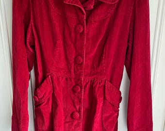 May include: A red corduroy jacket with a collared neckline, button closure, and two front pockets. The jacket has a fitted waist and long sleeves. The brand label "J.A.T." is visible on the front of the jacket.