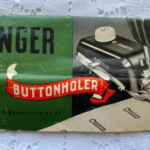 Puede incluir: Un accesorio vintage para ojal Singer para una máquina de coser. El accesorio es negro y plateado con una etiqueta verde y roja que dice "Singer Buttonholer" y "The Singer Manufacturing Co."