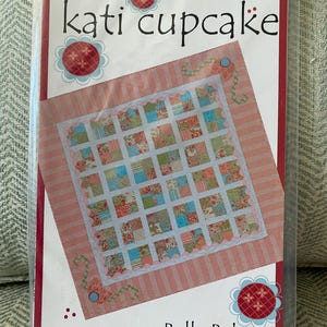 May include: A pink and white quilt pattern with a floral design. The pattern is called "Bella Baby" and is by "kati cupcake".