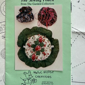 May include: A green brochure titled "The Sewing Pouch" from "The Garden Collection" features three sewing accessories. The brochure includes a pincushion with a floral design, and two drawstring pouches. The brochure also includes the Magic Mouse Creations logo.
