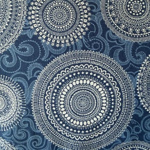 May include: Close-up of a fabric with a repeating pattern of white, circular mandala designs on a dark blue background. The design includes intricate details and swirling accents, creating a textured appearance.