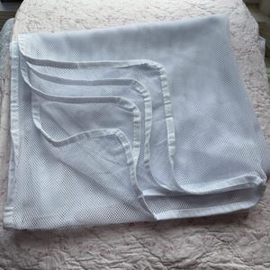 May include: A white mesh laundry bag with multiple compartments. The bag is folded and has a rectangular shape with rounded corners. The compartments are outlined with white trim. The bag is designed for washing delicate items.