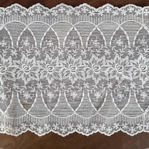 May include: A rectangular, off-white lace doily with a scalloped edge. The design features large floral motifs, delicate vines, and geometric patterns. This decorative piece is suitable for various home decor applications.