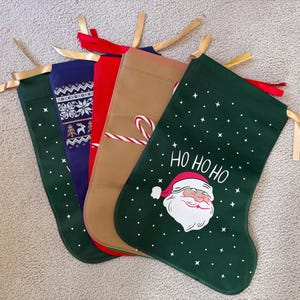 May include: A selection of Christmas stockings in different colours and patterns. The stockings include a dark green stocking with a Santa Claus graphic and the words "HO HO HO", a navy blue stocking with a white pattern, and a tan stocking with a candy cane.