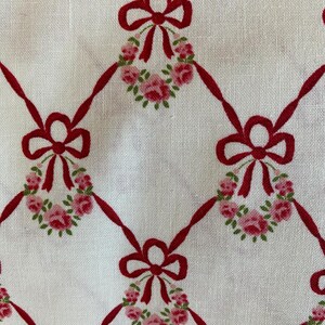Könnte beinhalten: Weißer Stoff mit einem sich wiederholenden Muster aus roten Schleifen und Kränzen aus rosafarbenen Rosen. Der Stoff hat eine Leinenstruktur.