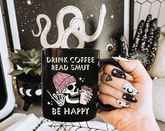 May include: Black coffee mug with a skeleton holding a coffee cup and the text "Drink Coffee Read Smut Be Happy".