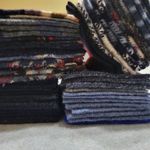 May include: A stack of blue and gray fabric squares, with a smaller stack of blue fabric squares in front. The fabric squares are all different sizes and have a soft, fuzzy texture.