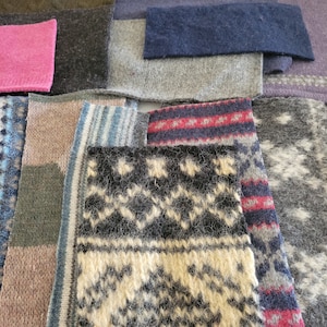 May include: A collection of various knitted fabric swatches in shades of gray, blue, pink, and beige. Some swatches feature patterned designs in contrasting colors, including geometric and striped patterns. The textures vary, showcasing the different knit styles.