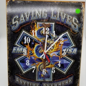 Puede incluir: Un reloj de pared con fondo negro y un diseño de estrella de la vida azul y blanca. La esfera del reloj presenta una serpiente con un símbolo médico rojo y blanco. La esfera del reloj también tiene las palabras "EMS" y "USA" en ella. El reloj está rodeado por las palabras "Saving Lives Anytime, Anywhere".