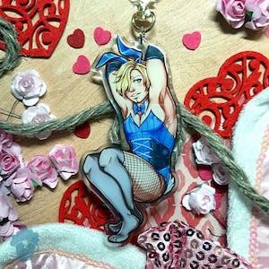 May include: A blue and white bunny costume charm with a blonde haired person wearing it. The charm is made of clear acrylic and has a black bow tie.