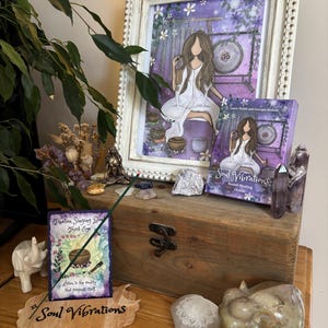May include: A framed print and a book titled "Soul Vibrations" are displayed on a wooden box, alongside decorative items. The print features a woman in white, with a gong in the background. The book cover has the same image. Other items include crystals, incense, and a wooden sign.