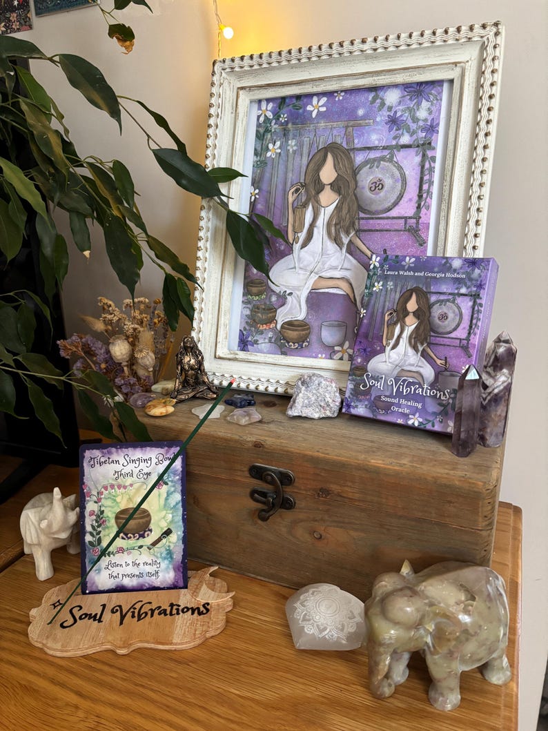 May include: A framed print and a book titled "Soul Vibrations" are displayed on a wooden box, alongside decorative items. The print features a woman in white, with a gong in the background. The book cover has the same image. Other items include crystals, incense, and a wooden sign.
