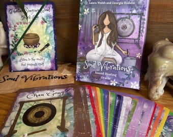 May include: A Soul Vibrations Sound Healing Oracle deck with a purple cover featuring an illustration of a woman and a gong. The deck includes cards with images of singing bowls and gongs. The text on the cards includes "Tibetan Singing Bowl" and "Chau Gong".