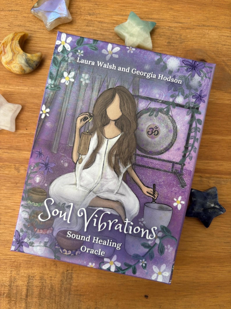 May include: A book titled "Soul Vibrations" with a purple cover featuring an illustration of a woman in white. The book is surrounded by star-shaped and crescent-shaped crystals. The text "Sound Healing Oracle" is also visible.