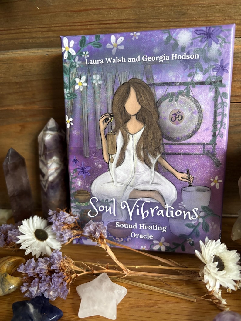 May include: A purple and white oracle card deck titled "Soul Vibrations" with the text "Sound Healing Oracle." The cover art features an illustration of a person in white clothing, a gong, and flowers. Amethyst crystals and flowers surround the deck.