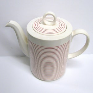 May include: White ceramic teapot with a red striped pattern and a lid with a circular handle.