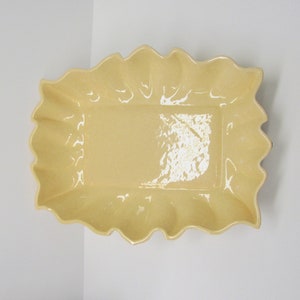 May include: A yellow ceramic serving dish with a scalloped edge. The dish is empty and ready to be filled with food.