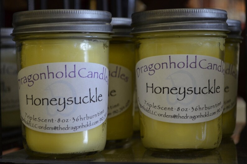 May include: Several Honeysuckle scented candles in glass jars with silver lids. Each candle has a label that reads "dragonhold Candles Honeysuckle". The candles are 8 oz and have a 36-hour burn time.