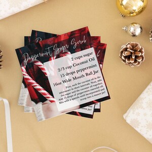 Peut inclure: Une carte rouge et noire à carreaux avec une canne en sucre à la menthe dessus. La carte contient des instructions pour faire un gommage au sucre à la menthe avec 2 tasses de sucre, 2/3 tasse d'huile de noix de coco, 15 gouttes de menthe poivrée et un bocal à large ouverture de 16 onces.