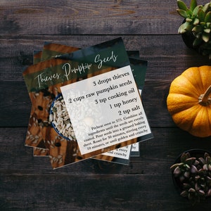 Może przedstawiać: Karta przepisu na nasiona dyni Thieves z listą składników, w tym nasiona dyni, olej do gotowania, miód i sól. Karta leży na drewnianej powierzchni z małą dynią i dwoma sukulentami.