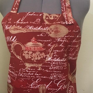 Beautiful red hand made Bib Apron with “Tea Time” and French script in gold lettering with tea cup, tea pot and tea spoon graphics.