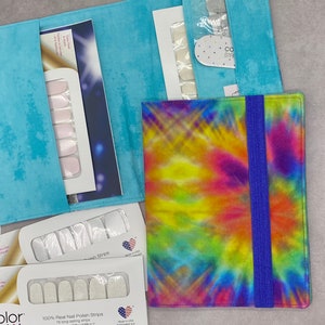 May include: A tie-dye fabric pouch with a blue elastic band closure. The pouch is designed to hold nail polish strips. The pouch is sitting on a table with several packages of nail polish strips.