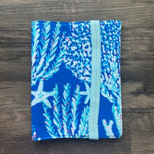 May include: A blue fabric book cover with a white and light blue coral reef pattern. The cover has a light blue elastic band closure.