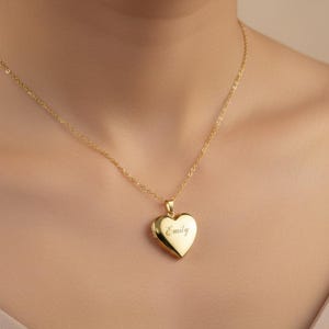Op de afbeelding: Een goudkleurige hartvormige medaillonhanger aan een fijne bijpassende ketting. Het vooroppervlak van het hartvormige medaillon is voorzien van de gegraveerde naam Emily in een cursief lettertype, gecentreerd op het gepolijste metalen oppervlak.
