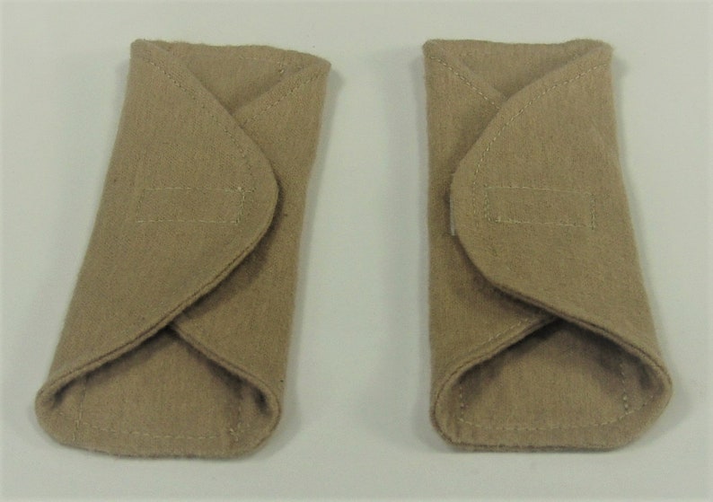 Puede incluir: Dos art&iacute;culos de fieltro beige, de forma rectangular con extremos redondeados. Cada uno tiene una solapa doblada y un detalle rectangular cosido. Se colocan uno al lado del otro sobre un fondo blanco.