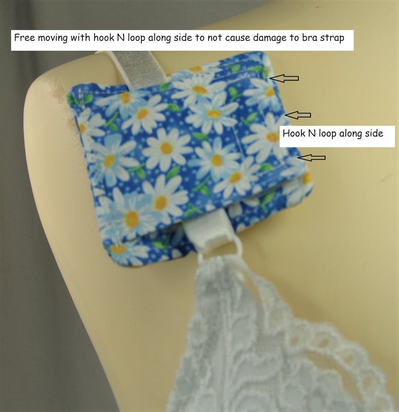 May include: A blue and white daisy print bra strap holder with the text "Free moving with hook N loop along side to not cause damage to bra strap". The holder is attached to a white bra strap.