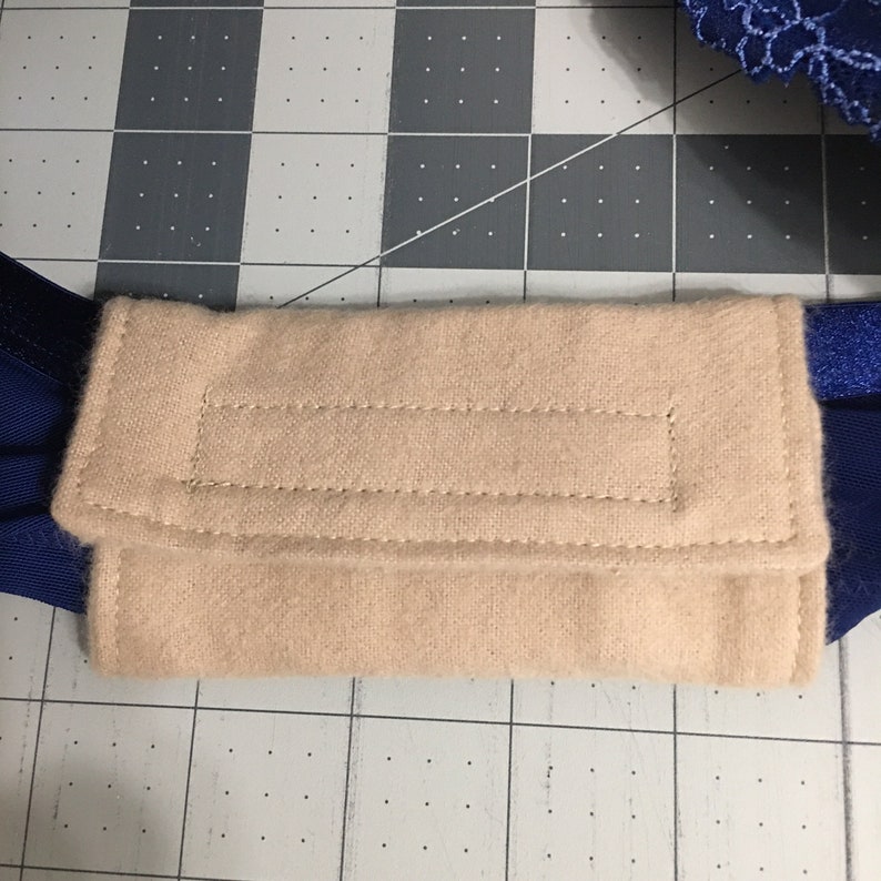 May include: A rectangular beige fabric strap pad with visible stitching along the edges, attached to a dark blue elastic strap. The pad features a soft, textured surface and is centred horizontally across the blue band, providing a cushioned layer.