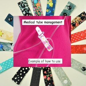 May include: A pink shirt with a clear medical tube secured with a pink and white daisy patterned tube holder. The text "Medical tube management" and "Example of how to use" is displayed on the image. The image also shows a variety of fabric tube holders with different patterns and colors.