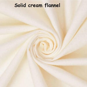 Puede incluir: Primer plano de tela de franela color crema, doblada para mostrar la textura y profundidad del material. Las palabras "Solid cream flannel" est&aacute;n impresas en la parte superior. La tela parece suave y acogedora, ideal para proyectos de ropa o decoraci&oacute;n del hogar.