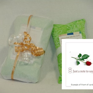 May include: A green fabric pouch with the text "Pillows that ease the ouch!" and a white card with a red rose and the text "Just a note to say..." and "Example of front of card".