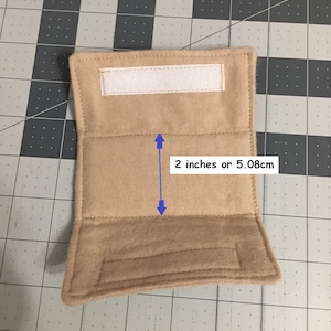 May include: A rectangular tan felt wrap featuring a white hook-and-loop fastener strip at the top and a matching strip at the bottom. A blue arrow graphic indicates a central section height of 5.08 cm or 2 inches between the stitched horizontal lines.