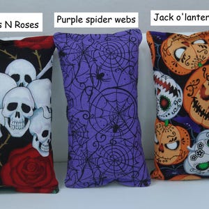 May include: Three Halloween-themed decorative pillows. One features skulls and roses, another purple spider webs, and the third Jack o'lanterns and sugar skulls. The pillows are rectangular and made of fabric.