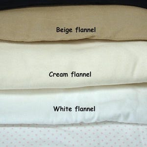 May include: A stack of five folded flannel fabric swatches labelled with text. The colours include black, beige, cream, and white, with the bottom swatch featuring a white and pink polka dot pattern. The labels read Black flannel, Beige flannel, Cream flannel, White flannel, and White N Pink flannel.