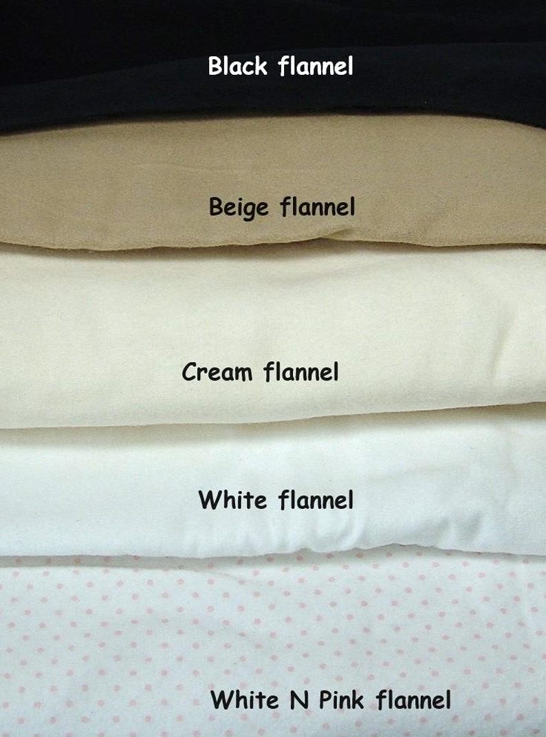 May include: A stack of five folded flannel fabric swatches labelled with text. The colours include black, beige, cream, and white, with the bottom swatch featuring a white and pink polka dot pattern. The labels read Black flannel, Beige flannel, Cream flannel, White flannel, and White N Pink flannel.