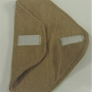 Puede incluir: Un art&iacute;culo de tela beige con forma curva, con dos cierres de velcro blancos. El art&iacute;culo parece estar doblado, con costuras visibles en los bordes. La tela tiene un aspecto suave y texturizado.
