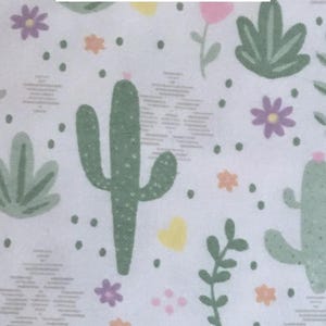 Puede incluir: Una tela de franela blanca con un patr&oacute;n repetitivo de cactus verdes, flores moradas, corazones amarillos y peque&ntilde;as flores naranjas. El texto "catus flannel" est&aacute; impreso en letras negras en la parte superior central del patr&oacute;n.