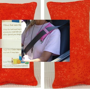 May include: Two orange pillows with a white floral pattern. The pillows are made from cotton fabric and have hook and loop tape. The text on the pillow reads: "Pillows that ease the Wrap the hook and loop t around your seat belt wit pillow against your body/ Made from Cotton fabric and hook N loop tape. Louise Perkin Etsy.com/shop/LouisesSewingBasket"