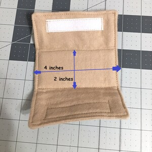 May include: A tan rectangular fabric pouch featuring a white hook-and-loop fastener strip along the top edge. The pouch has a width of 10.16 cm and a height of 5.08 cm, indicated by blue arrows and text labels printed directly on the item.